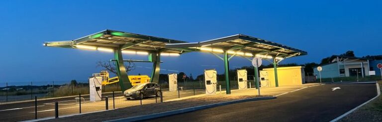 Station de recharge rapide pour voitures électriques sous ombrière solaire, de nuit.