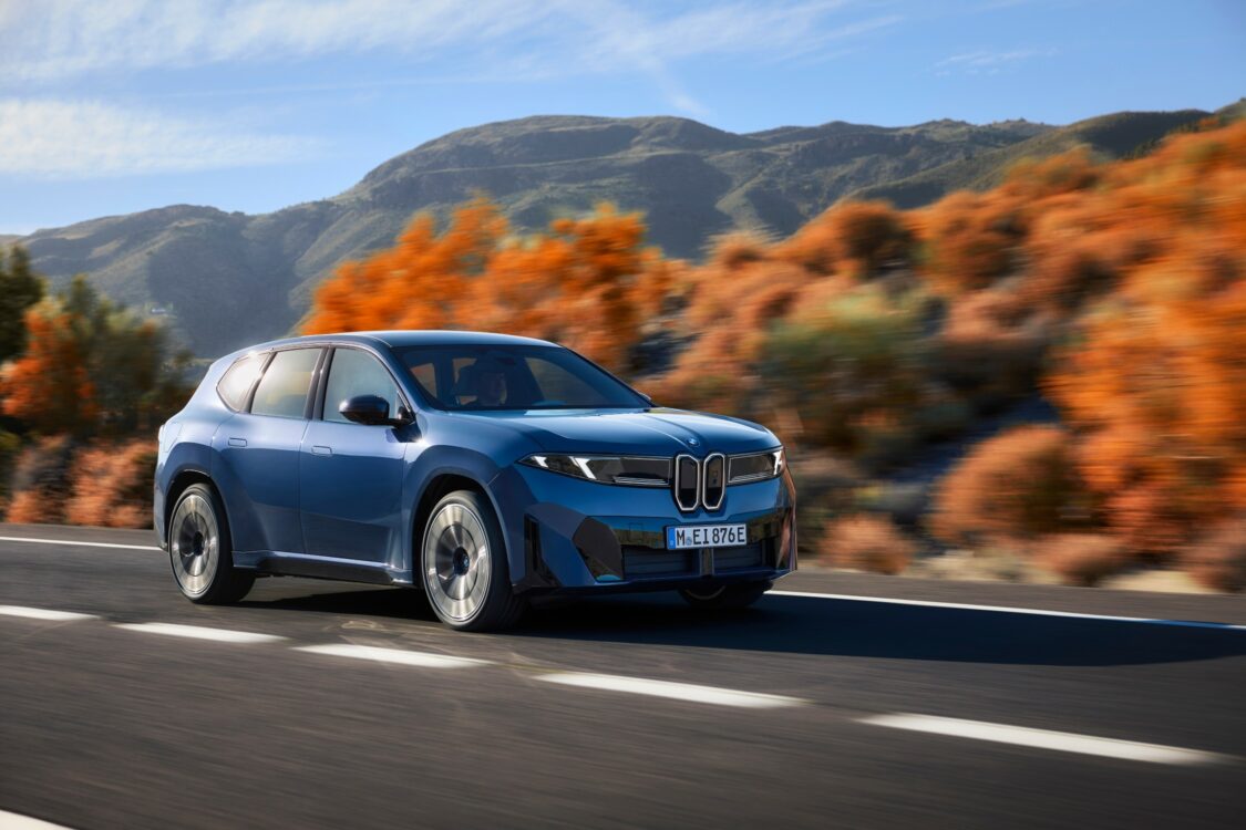 BMW iX3 – le SUV électrique en mouvement BMW iX3 en mouvement sur une route bordée de collines et de végétation automnale