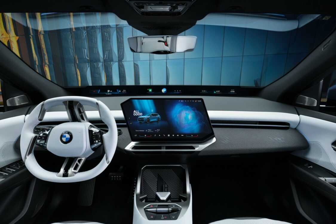 BMW iX3 – tableau de bord avec écran central multimédia Intérieur BMW iX3, tableau de bord avec volant blanc et écran central numérique affichant l’interface multimédia et un globe stylisé