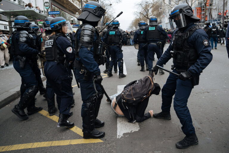 Des policiers en tenue de maintien de l’ordre interviennent autour d’un manifestant au sol à Paris.
